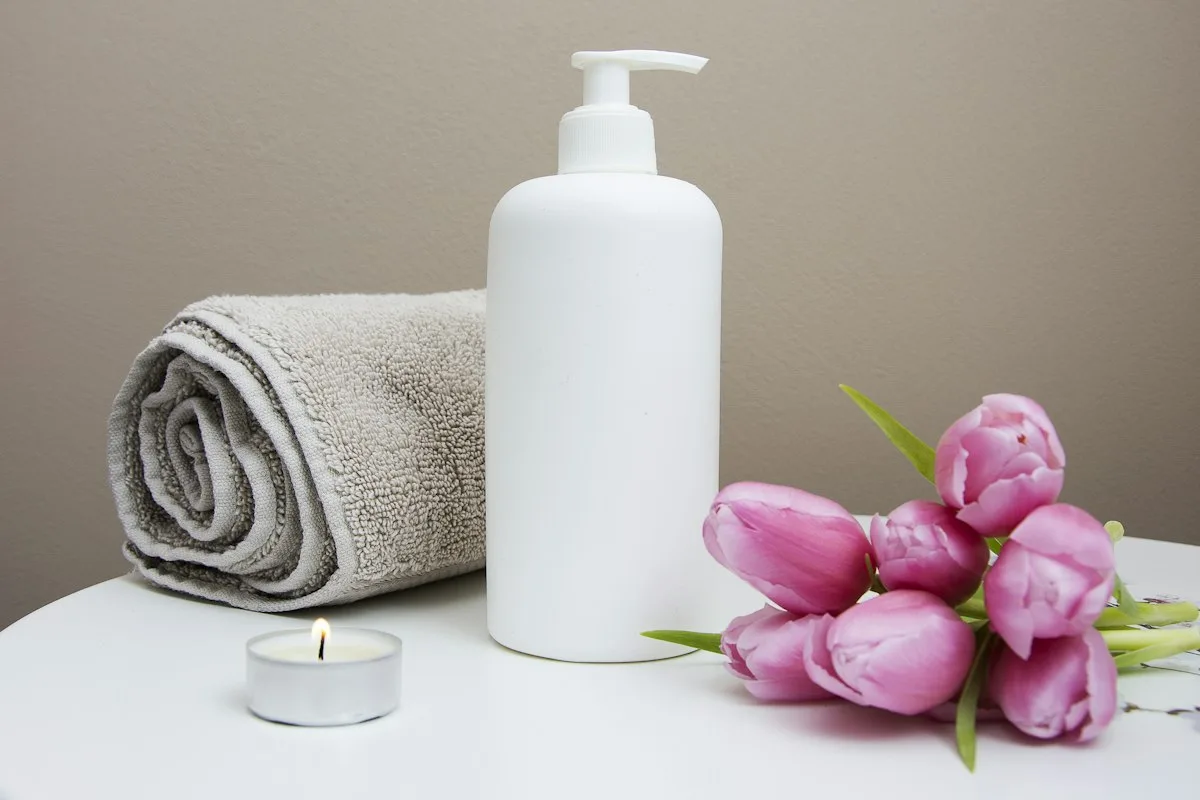 Natural bamboo bathtub caddy tray holding scented candle bar soap and book over white tub