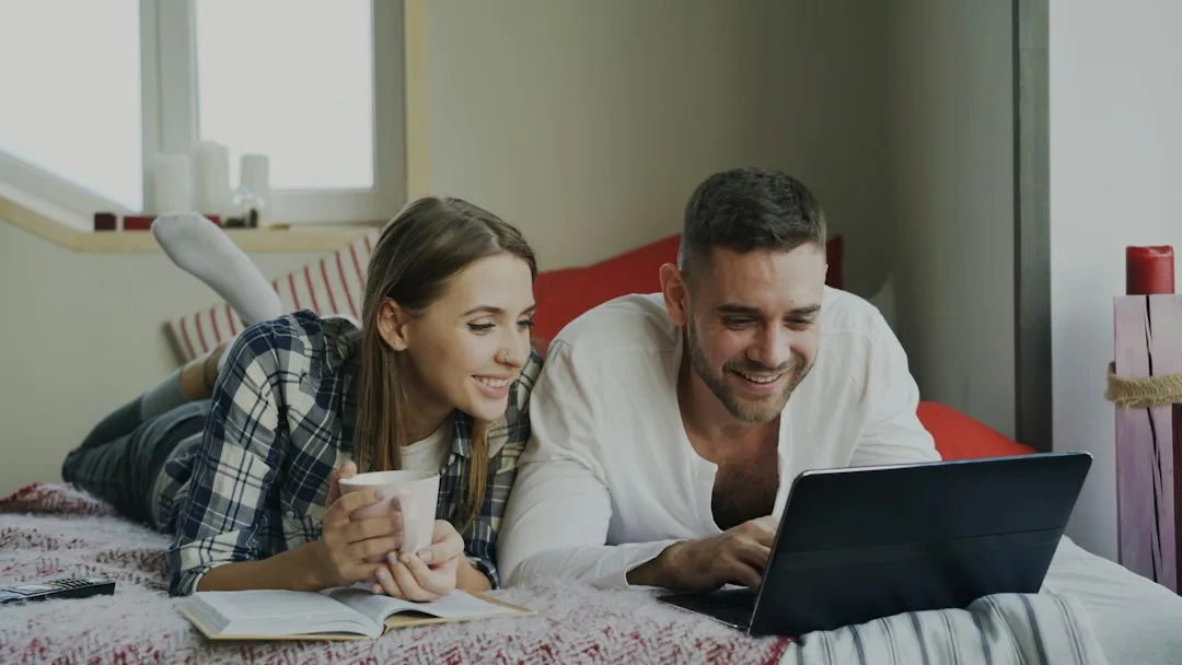 Young couple sitting together at desk reviewing household expenses notebook and calculator