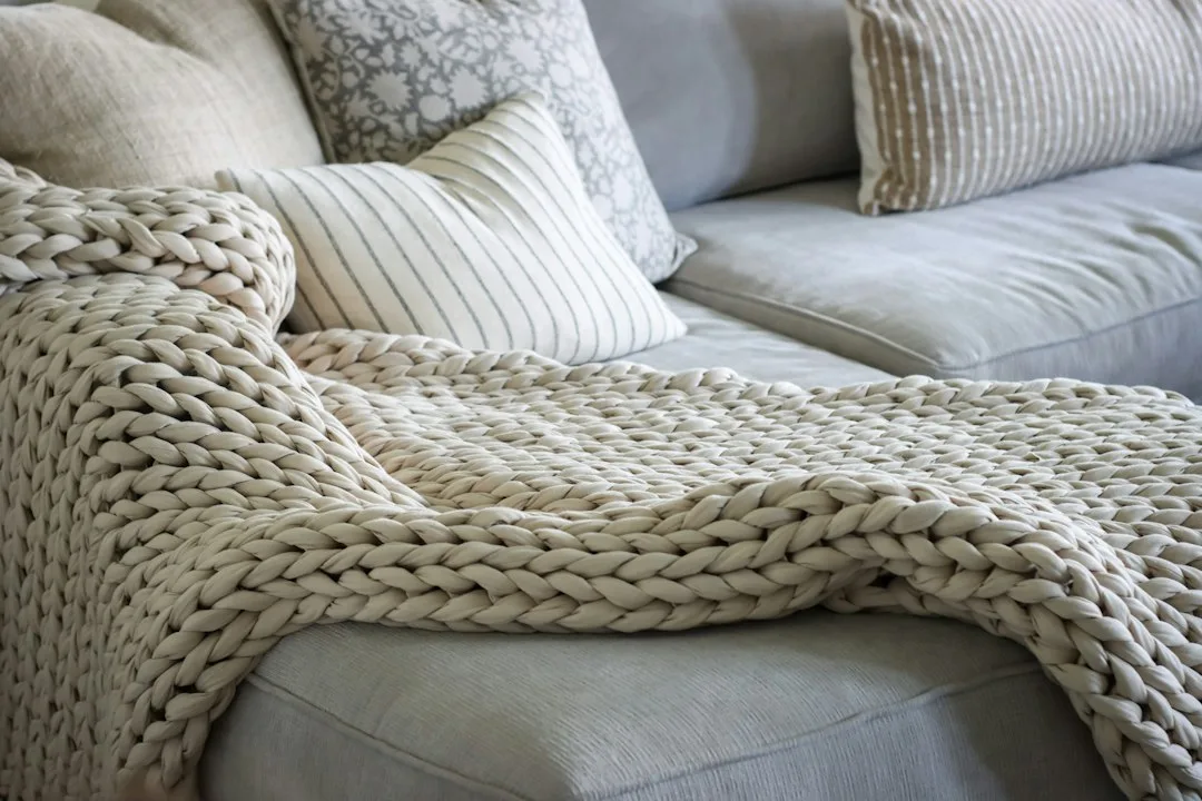 Folded warm knit wool blanket resting on sofa cushion in cozy winter living room