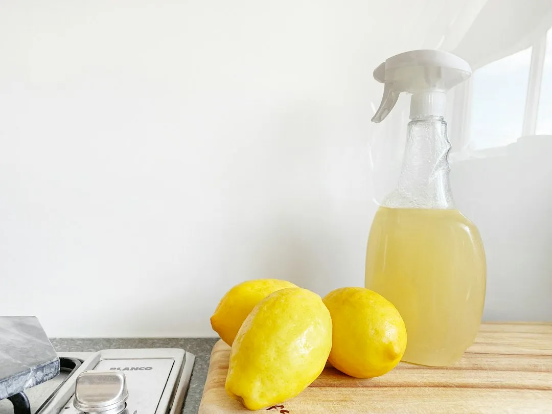 Glass bottle containing infused citrus peel vinegar spray beside fresh lemon slices