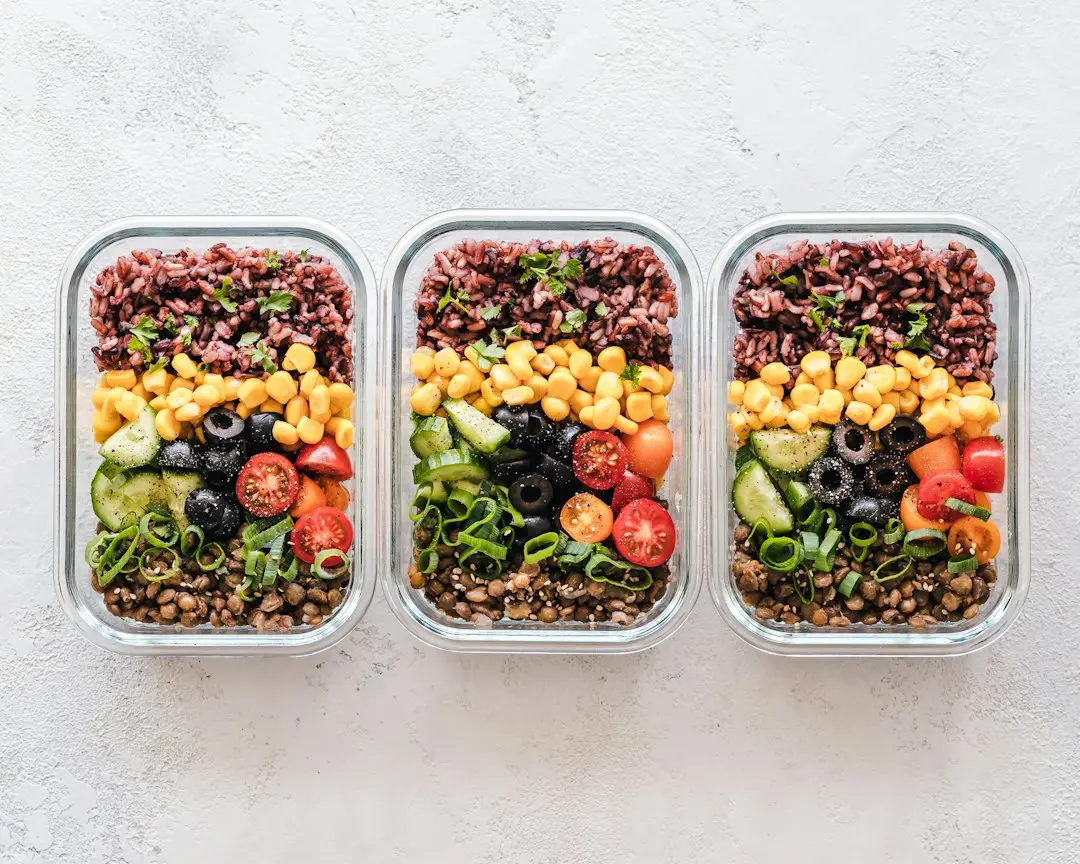 Row of glass food containers stacked with balanced home cooked meals and vegetables