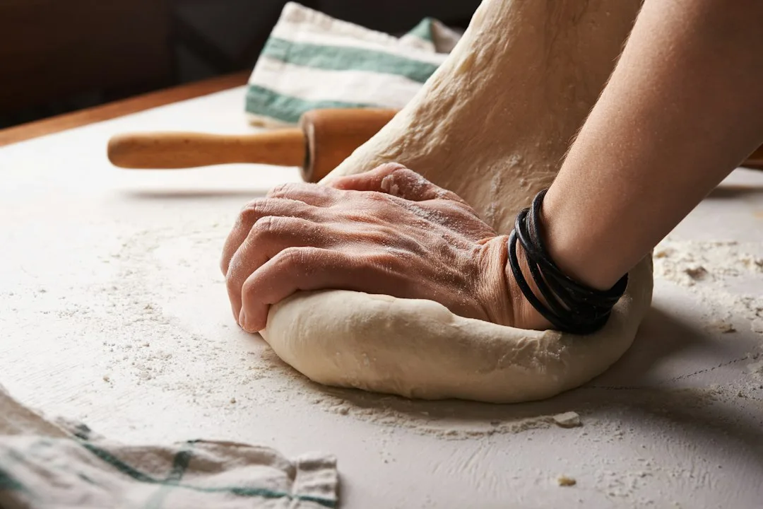 Fresh bread dough kneaded on rustic wooden counter with flour and simple kitchen tools
