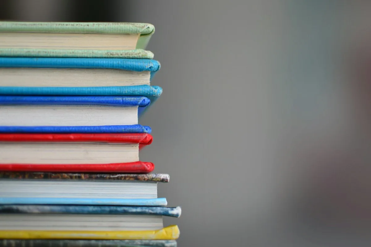 Stack of colorful hardback books borrowed from public library resting on wooden table