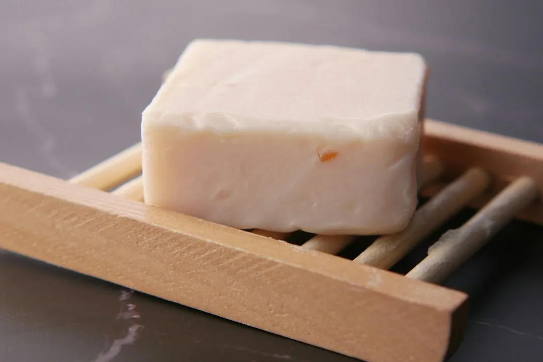 Square organic bar soap resting on slatted wooden dish in minimal white bathroom