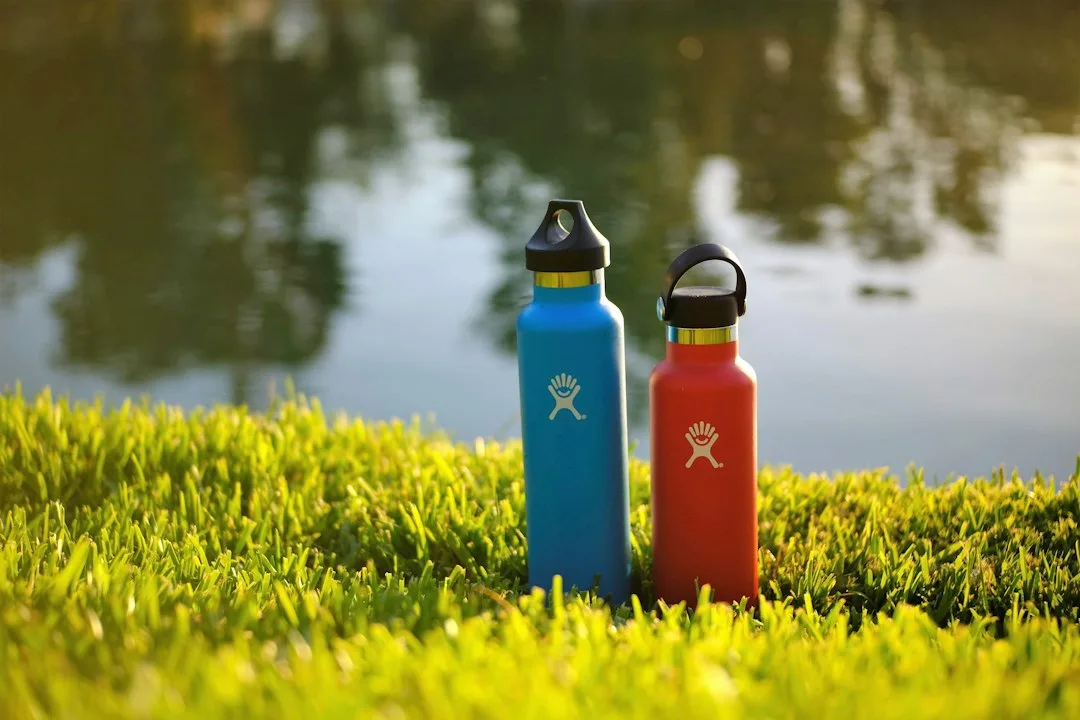 Stainless steel reusable water bottle resting on stone ledge in scenic outdoor sunlight