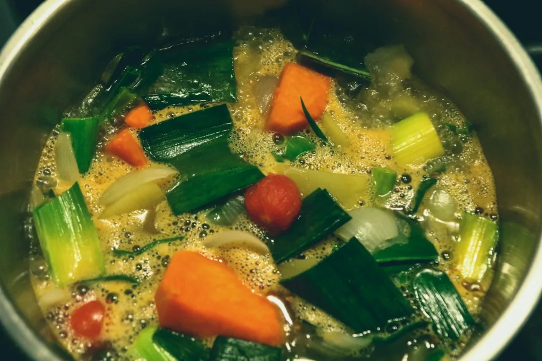 Stainless steel cooking pot simmering hot vegetable soup broth with fresh kitchen herbs