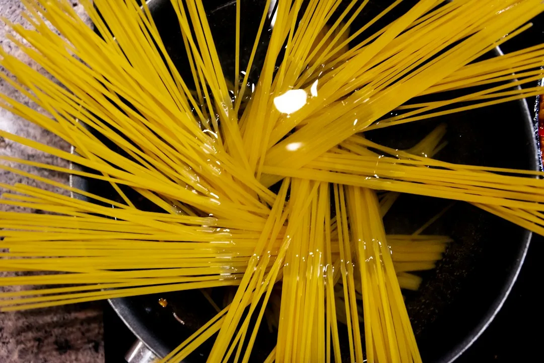 Steaming skillet of spaghetti pasta tossed with golden garlic flakes and fresh green parsley