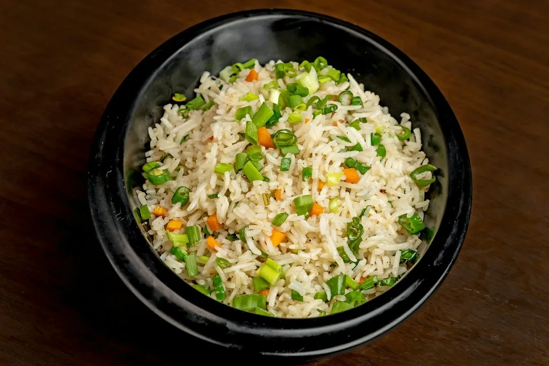 Steaming wok skillet filled with golden egg fried rice peas carrots and green onions