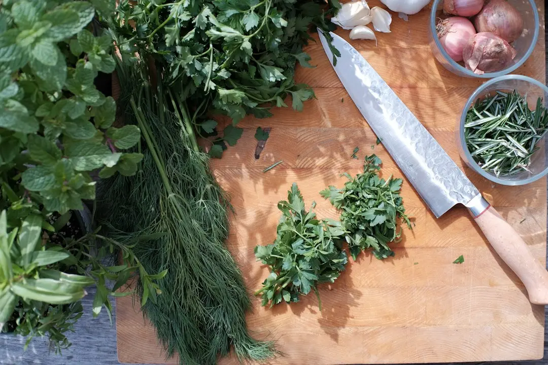 Wooden cutting board with fresh green herbs sliced red onions and whole garlic cloves